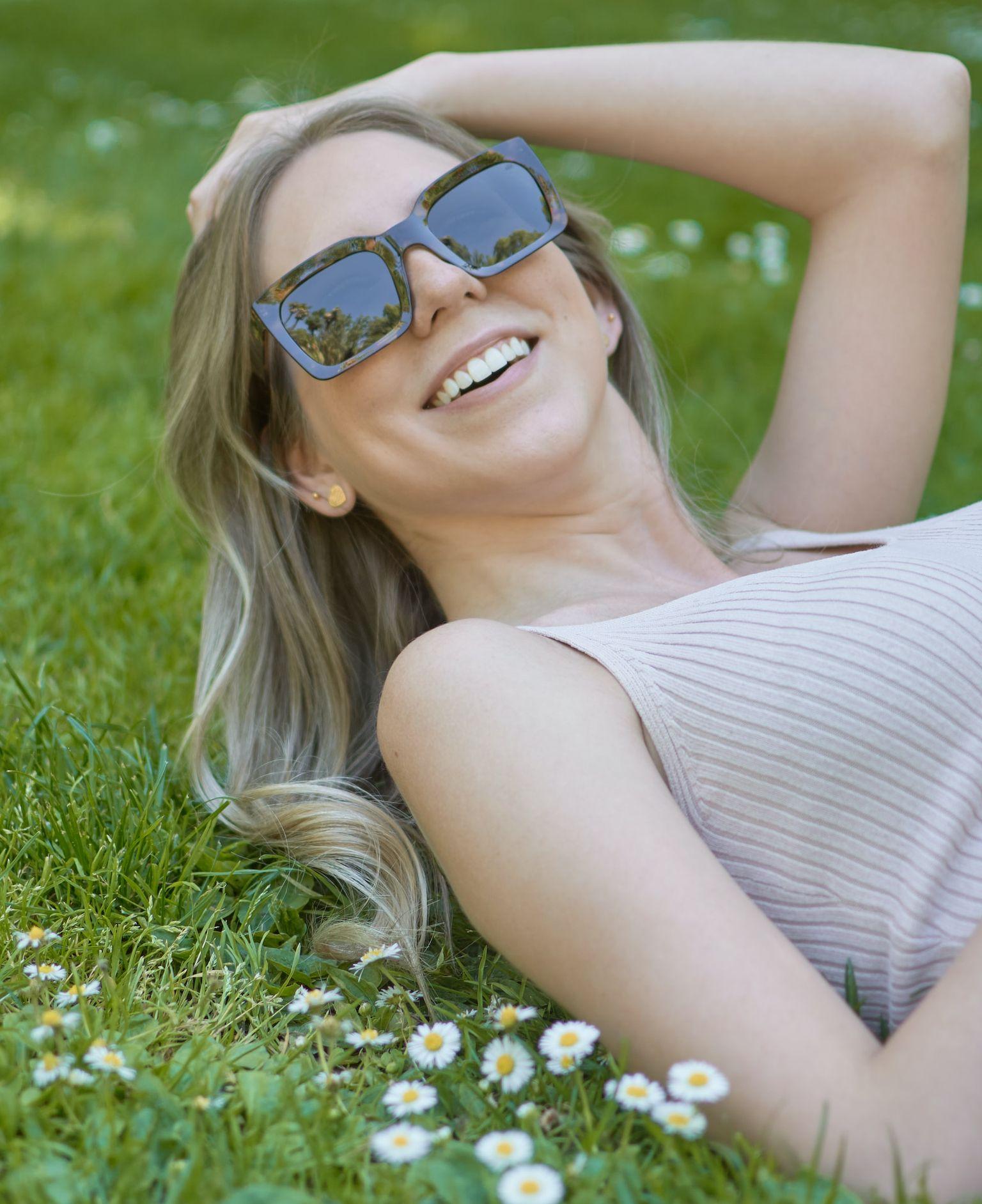 woman in white and black stripe tank top wearing blue sunglasses lying on green grass field